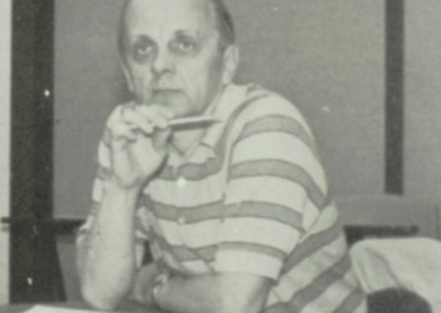 Ron Underwood seated at his desk at Beyer High School in the 1980s, holding a pen thoughtfully as he reviews student work.